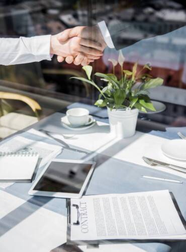 cropped shot of business partners shaking hands above contract